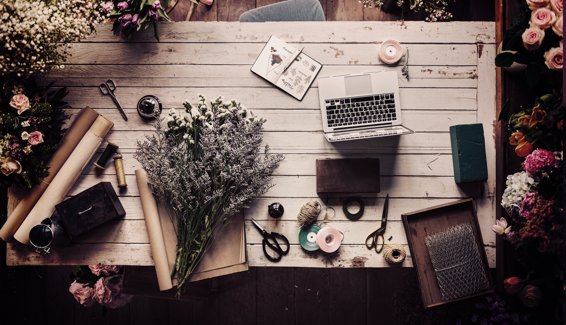 array of flowers and laptops on table in mood board style