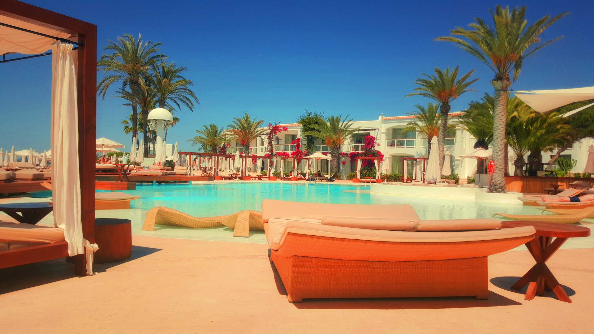 A high end hotel pool area with chairs and palm trees