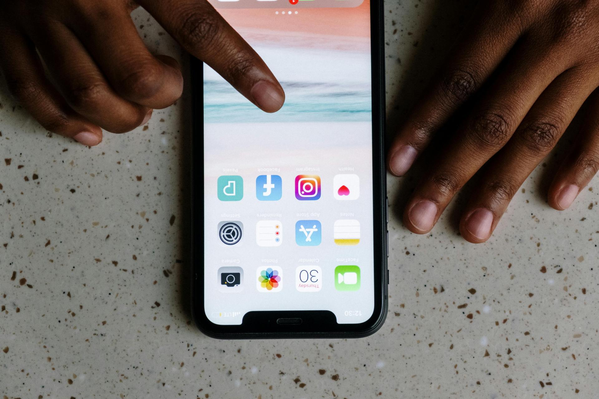 Fingers tap iPhone with apps on home screen.