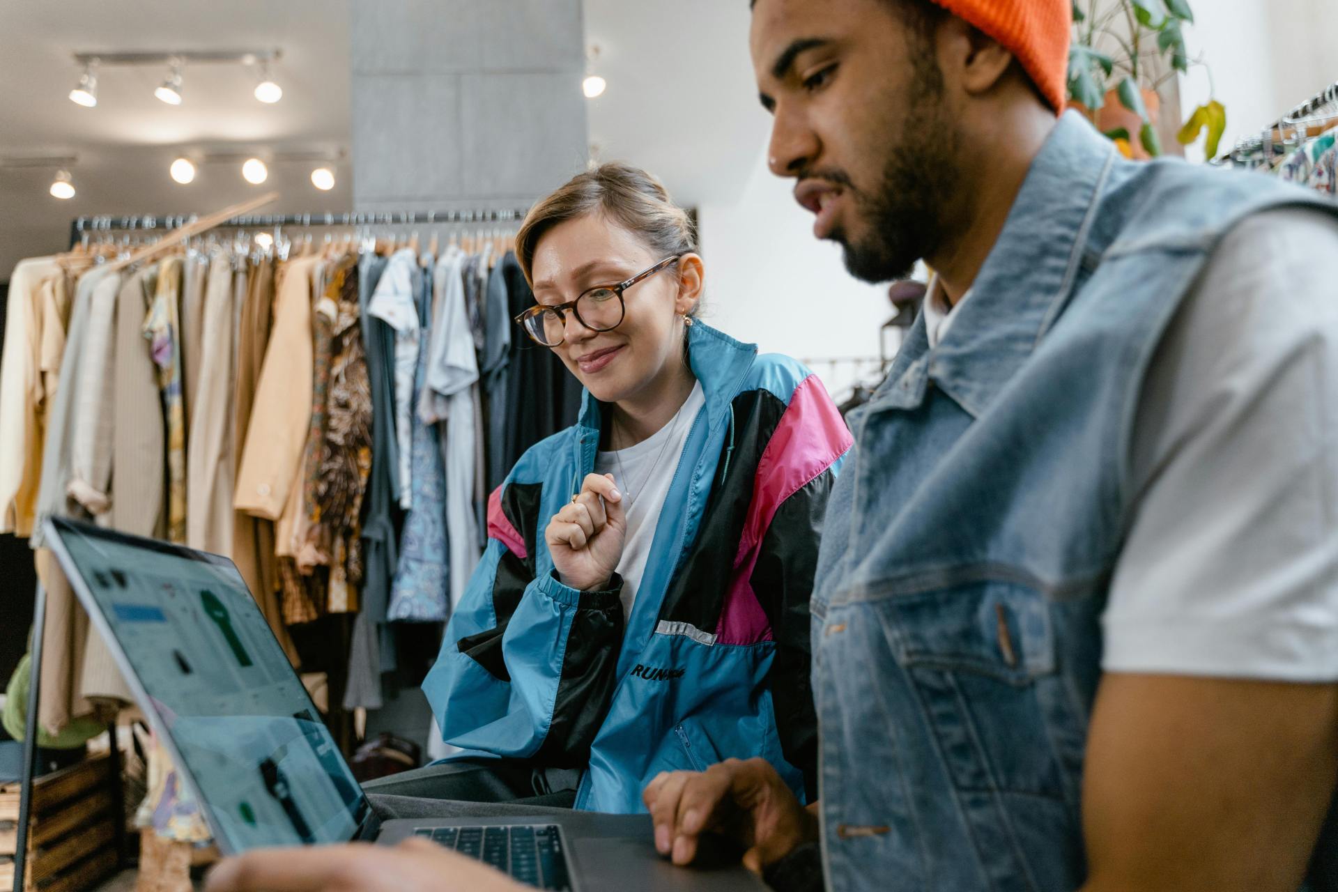 Man and woman collaborating on a laptop in a clothing store.