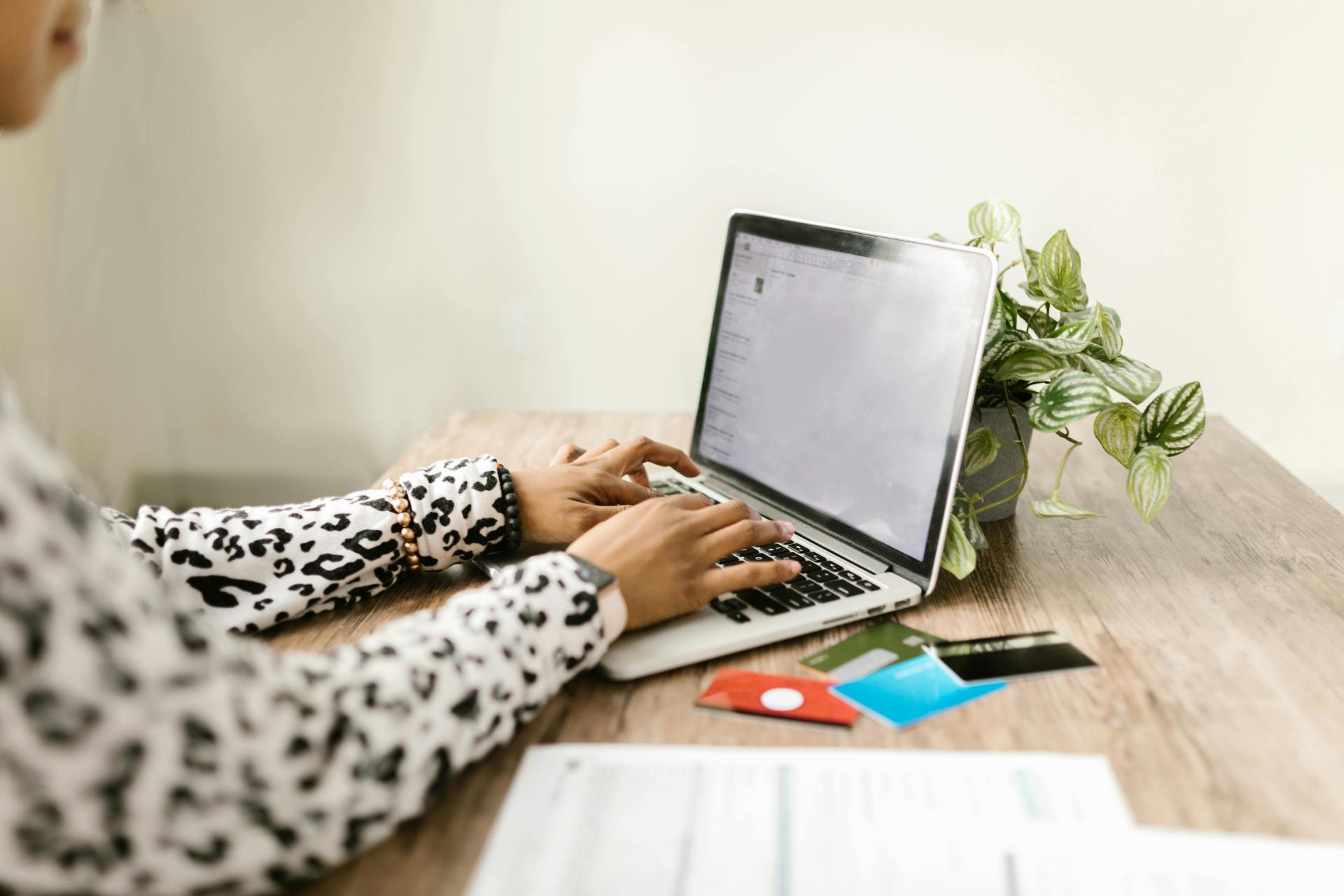 Woman typing on laptop with credit cards on a wooden desk.