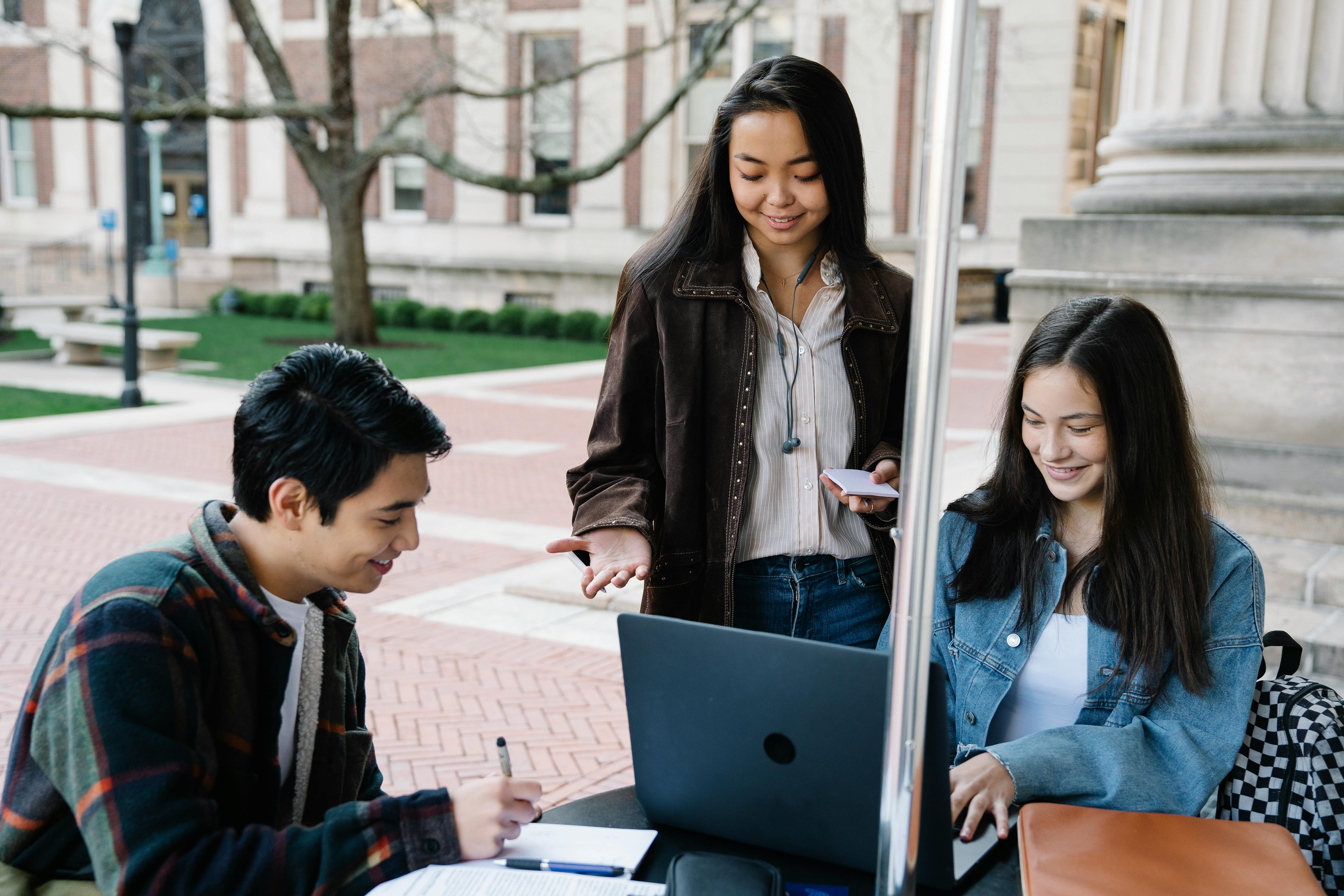 students stand around laptop on campus