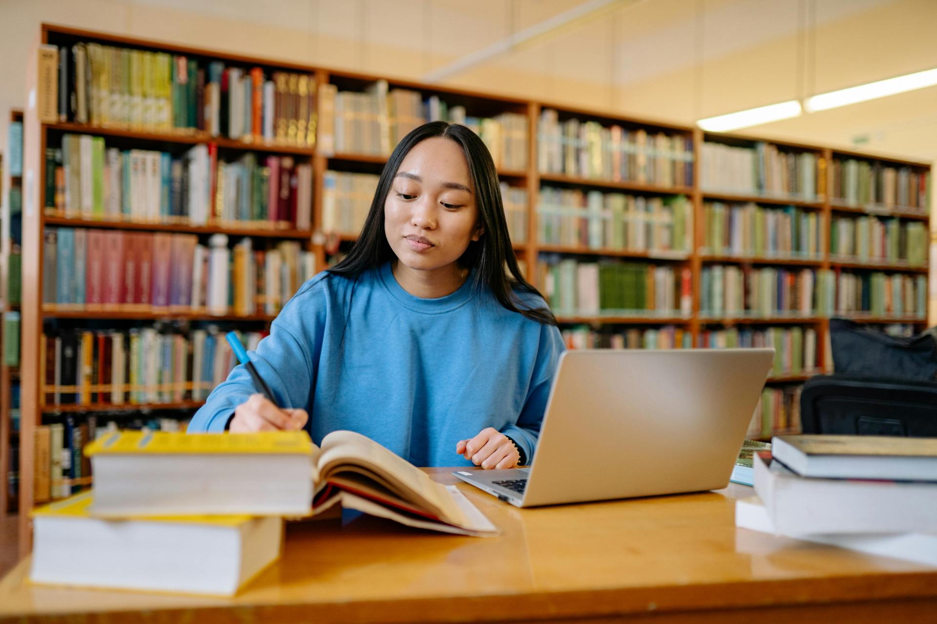 student sits with laptop and books in library