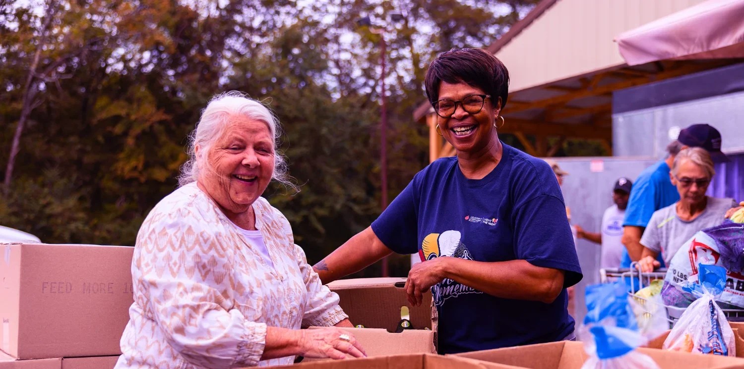 Two volunteers at Feed More separate food into boxes.
