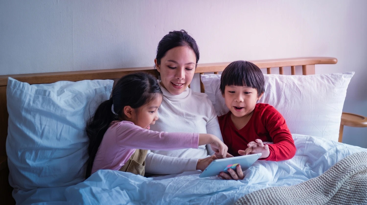 Two kids sit with their mom, interacting with an iPad.